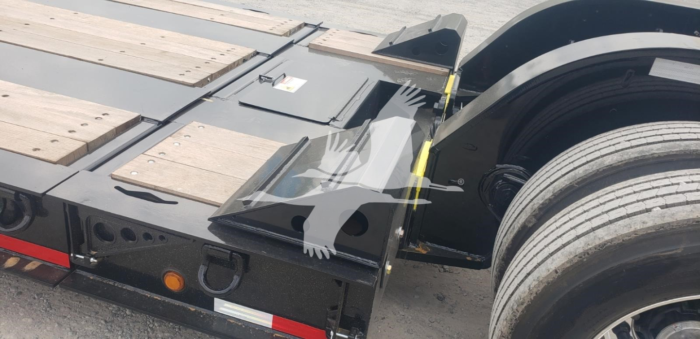 Lowboy trailer shows wooden deck boards, metal fender, and wheel hub area; visible components include chassis frame, ramps, and edge guards.