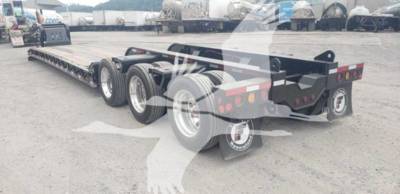 Fontaine 55Mx lowboy trailer showing aluminum gooseneck and long flatbed with tandem axles and rear deck, visible in yard.