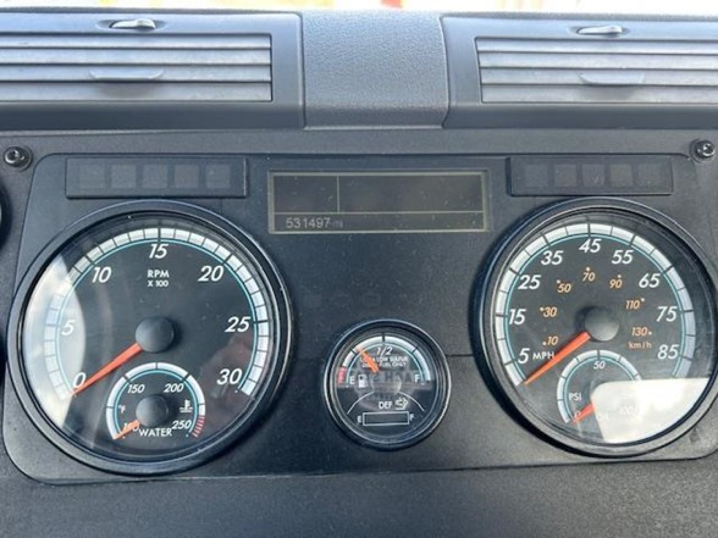 Dashboard of a Freightliner Cascadia truck showing two large gauges (tachometer and speedometer), a smaller center gauge, and warning lights/odometer area.