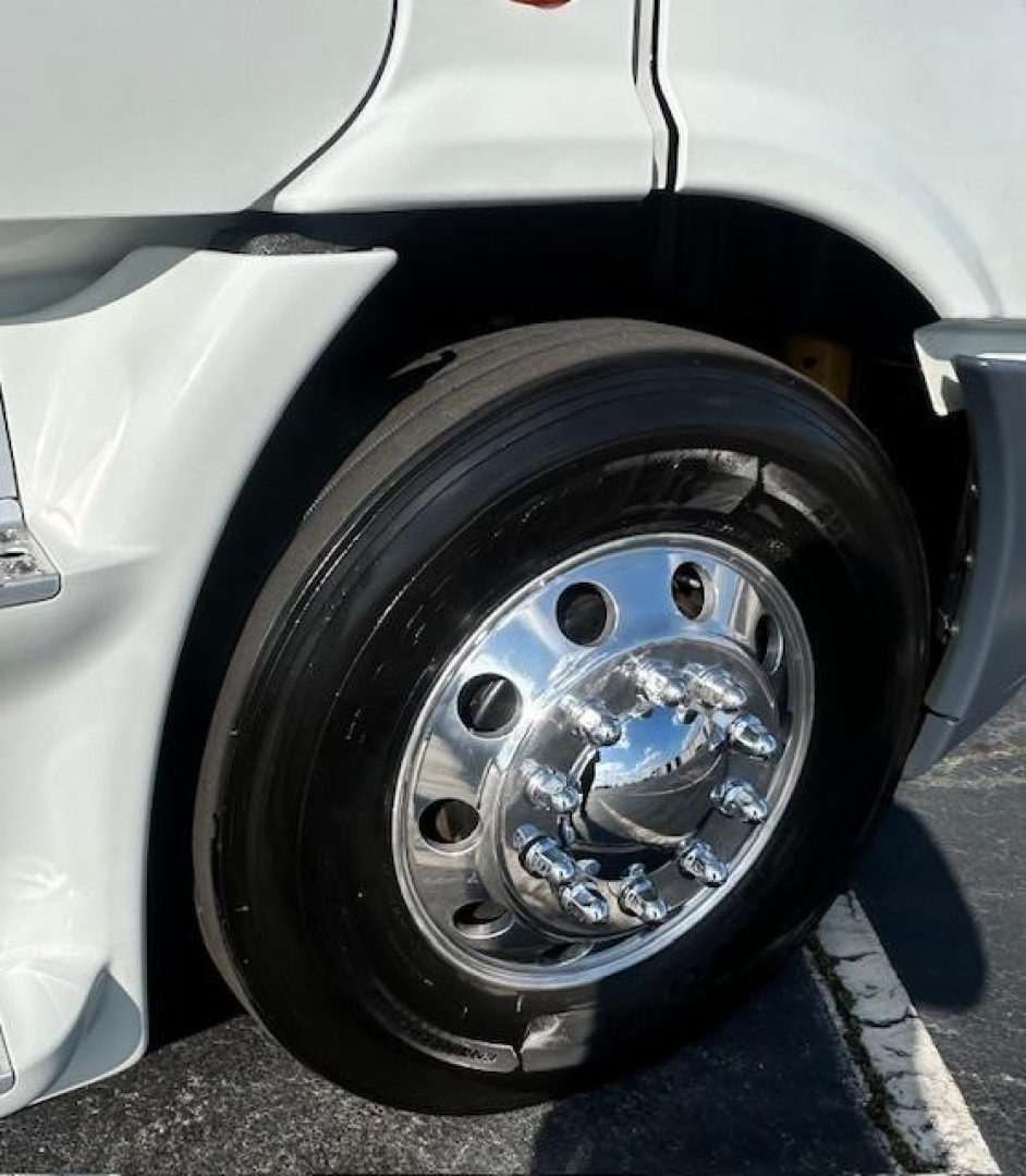 Truck front wheel and fender of a Freightliner Cascadia Evolution 2016 showing polished chrome hub, black tire, and white body panel.