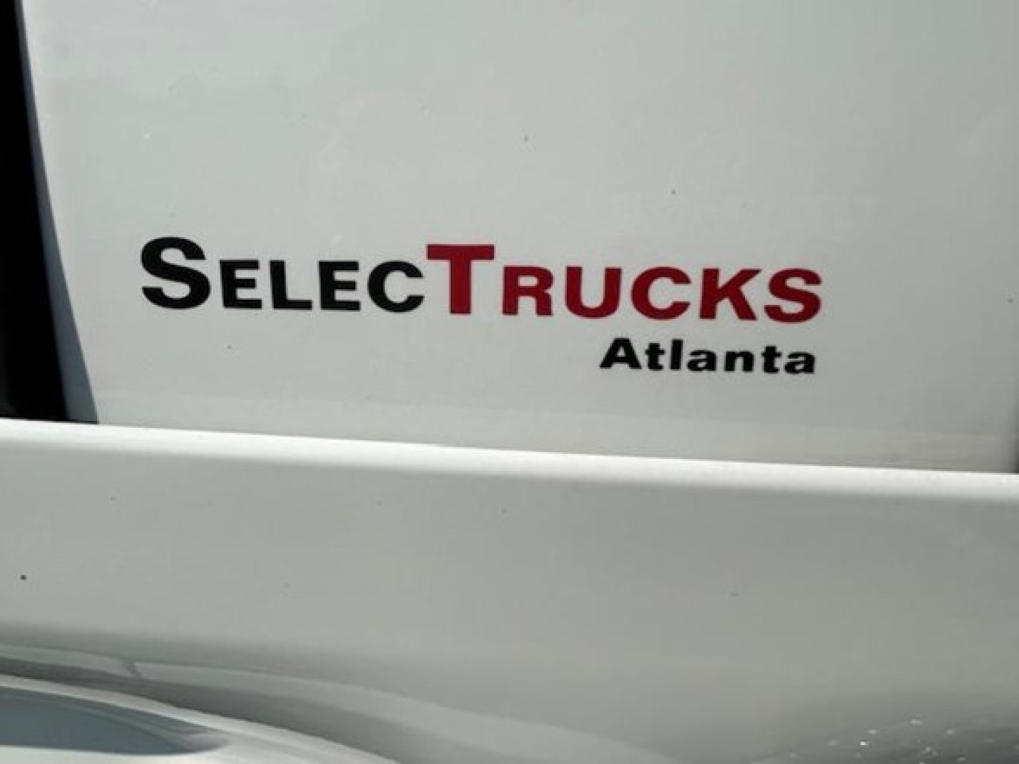 SelectTrucks Atlanta logo on a white vehicle surface with partial window and light reflections.