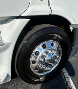 Truck front wheel and fender of a Freightliner Cascadia Evolution 2016 showing polished chrome hub, black tire, and white body panel.