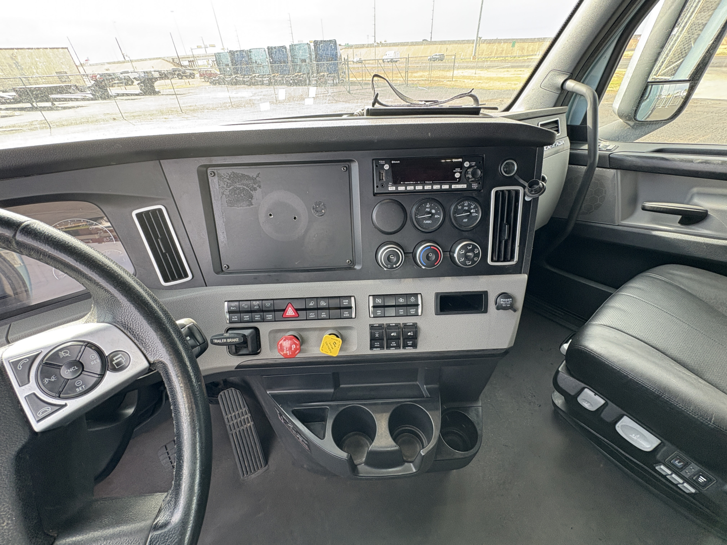 Cab interior of a Freightliner Cascadia 126 truck showing dashboard and steering wheel with gauges, controls, and cup holders.