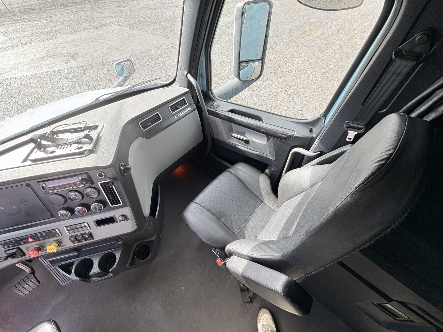 Cab interior of a 2023 Freightliner Cascadia 126 sleeper tractor showing steering wheel, dashboard, and driver's seat with window and mirror views.