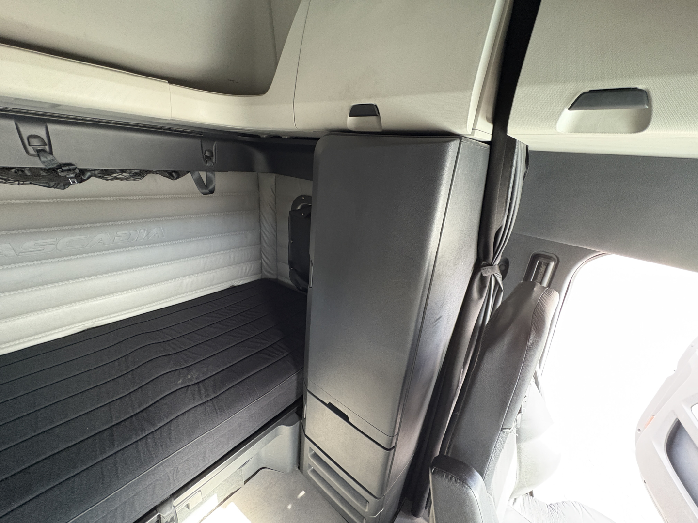Tractor-trailer cab interior showing sleeper bunk area with window and storage, no legible brand text visible on panel.