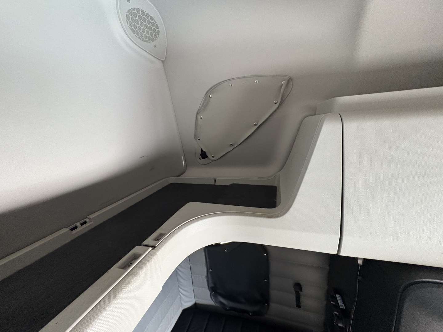 Truck cab interior corner with light gray panels and a rounded access panel; speaker grill visible on upper left; curved doorway and floor edge.