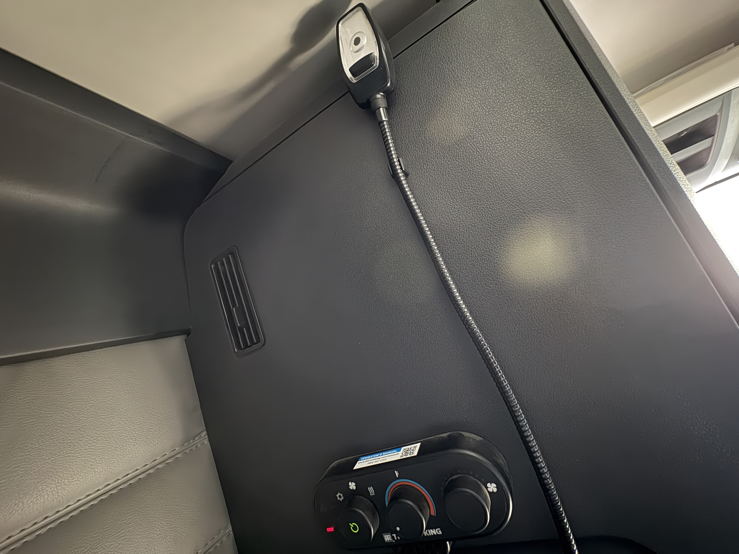 Cab interior of a Freightliner Cascadia 126 showing a small panel with a coiled cable and circular climate control dials.