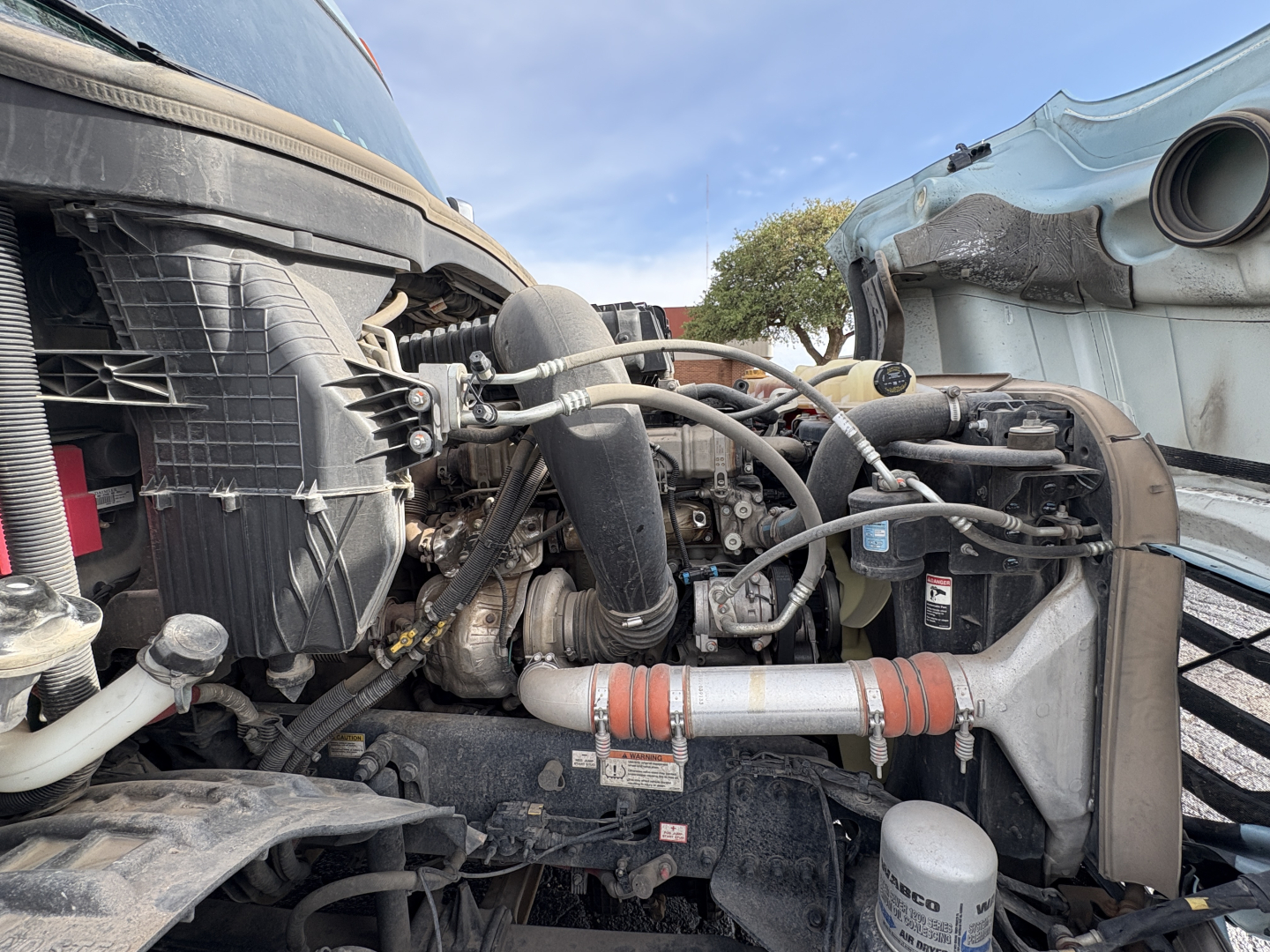 Front engine bay of a Freightliner Cascadia 126 truck showing radiator, turbo piping, hoses, and coolant reservoir with visible engine components.