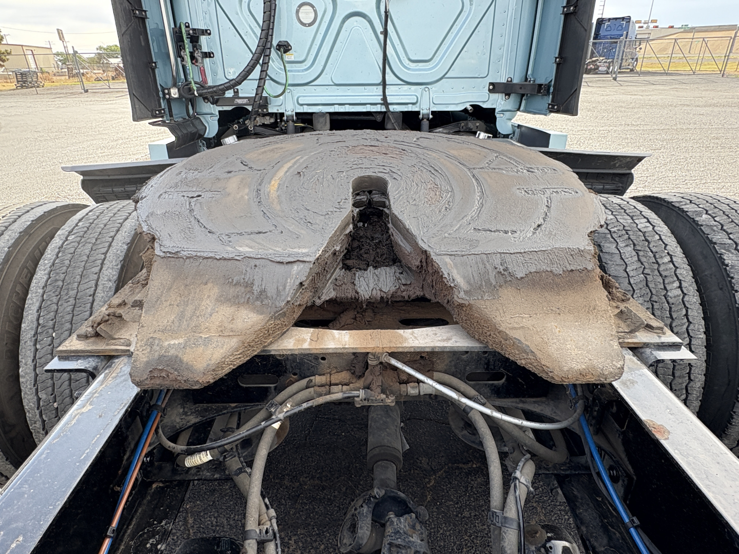 Freightliner Cascadia 126 drivetrain view showing fifth-wheel plate and rear chassis with hoses and cables; mud and wear around the fifth-wheel area.