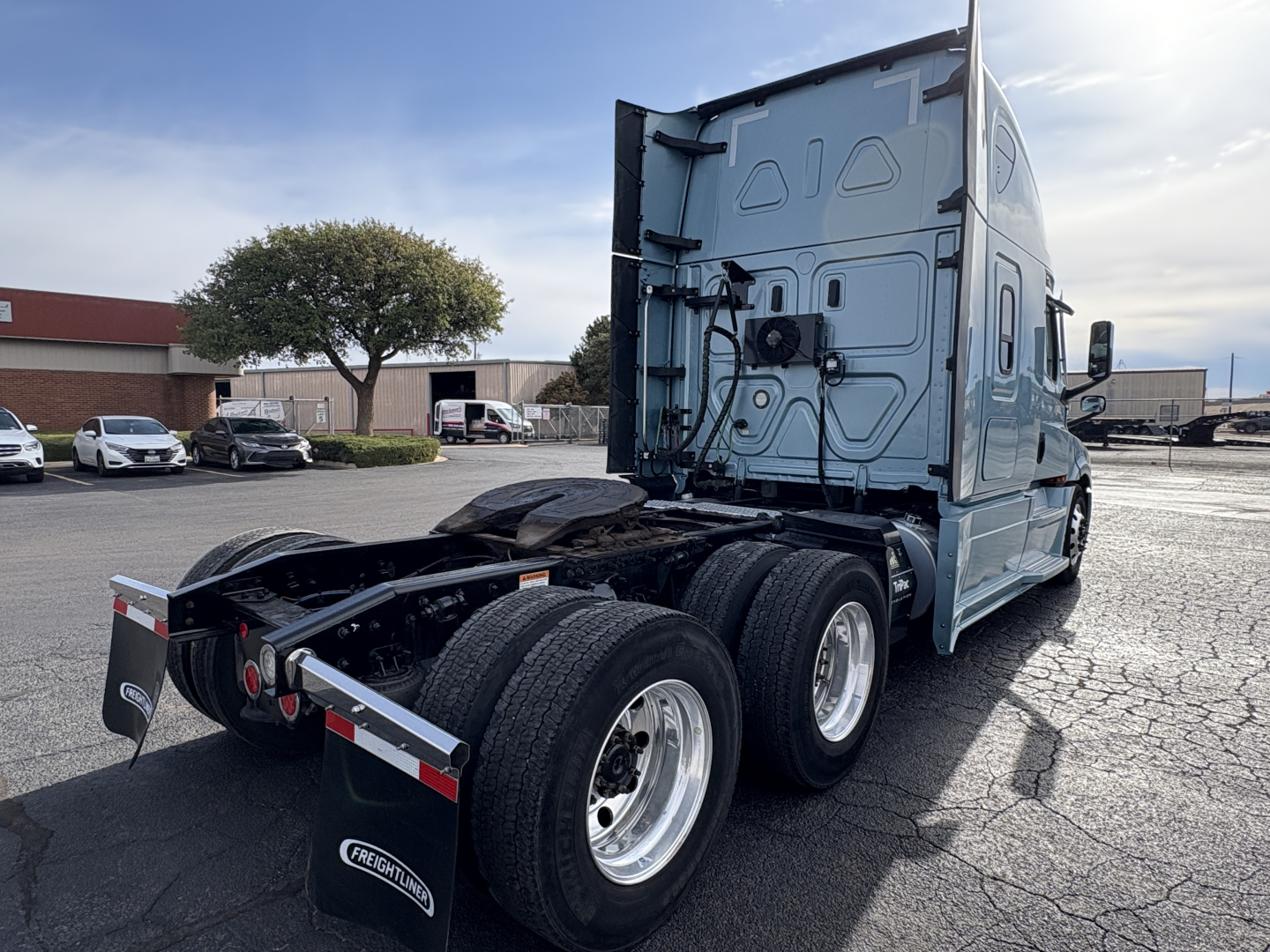Freightliner Cascadia 126 tractor rear view showing triple rear axles, fuel tank, and chassis with fifth wheel. No visible text legible on components.