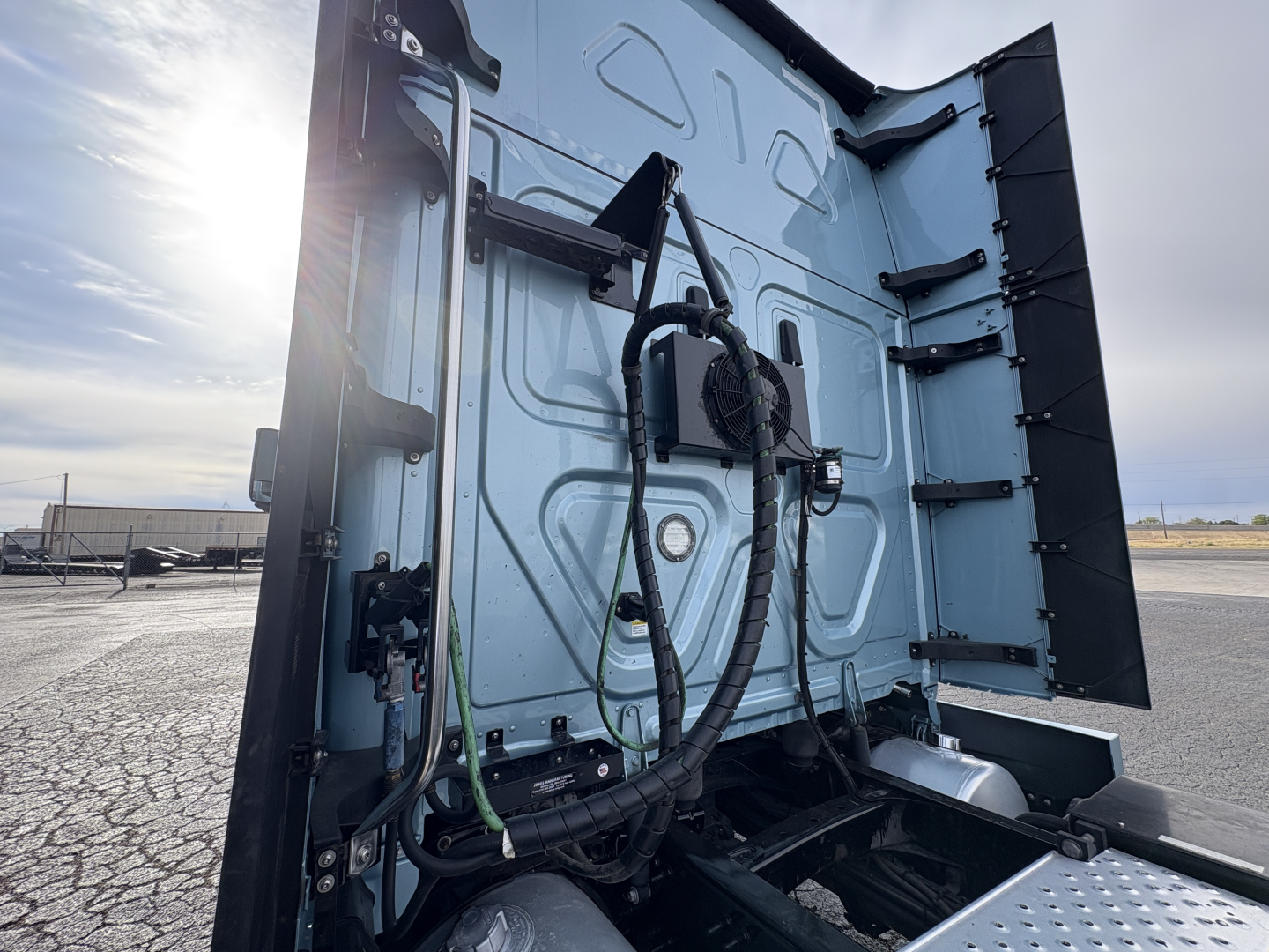 Freightliner Cascadia 126 truck rear cab area showing electrical cables and connectors, metal panels, hydraulic lines, and rear step surface.