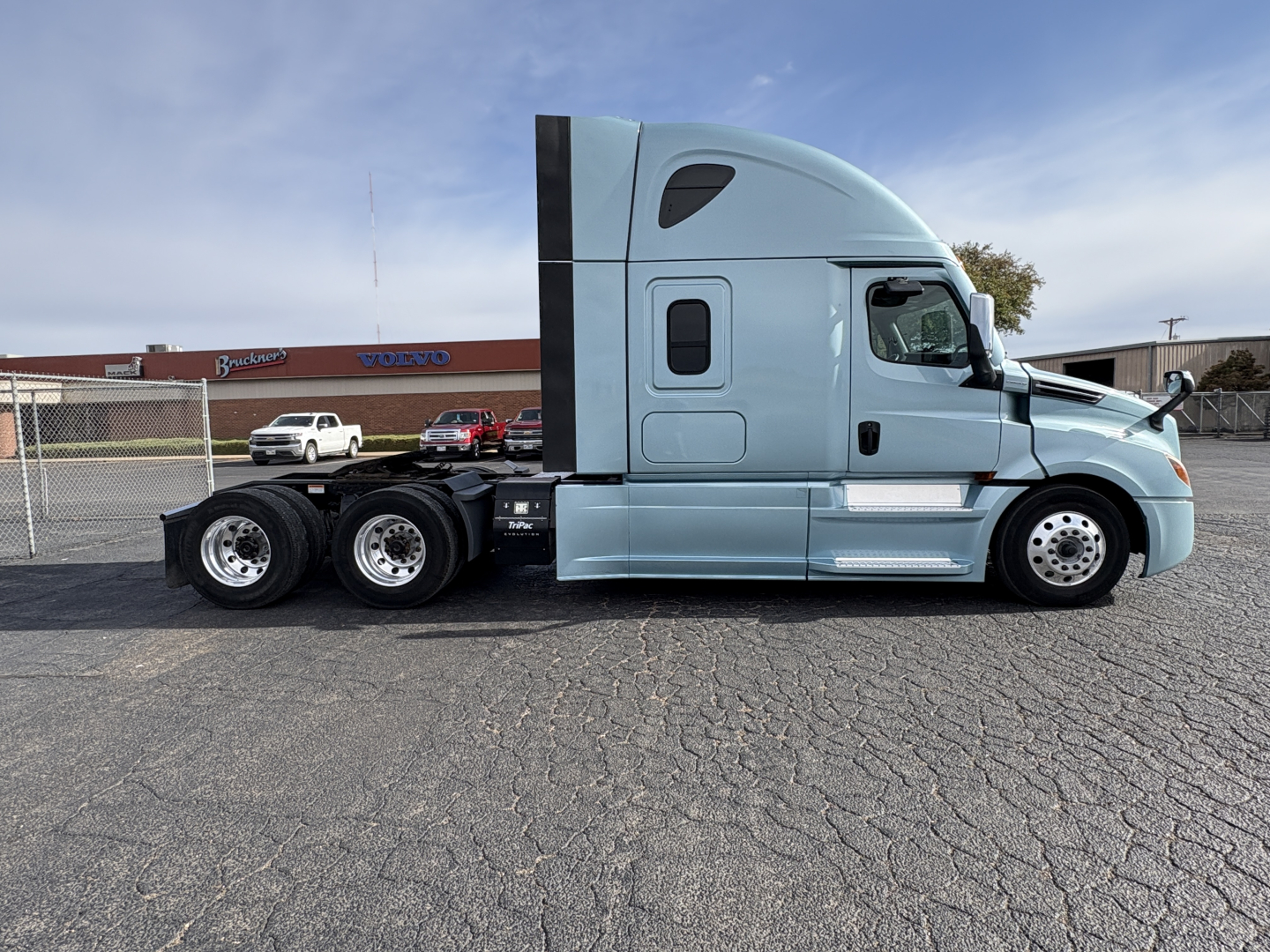 Semi tractor cab side view showing Freightliner Cascadia 126 with light blue paint, three rear axles, aerodynamic sleeper cab, side mirrors, and chrome steps.