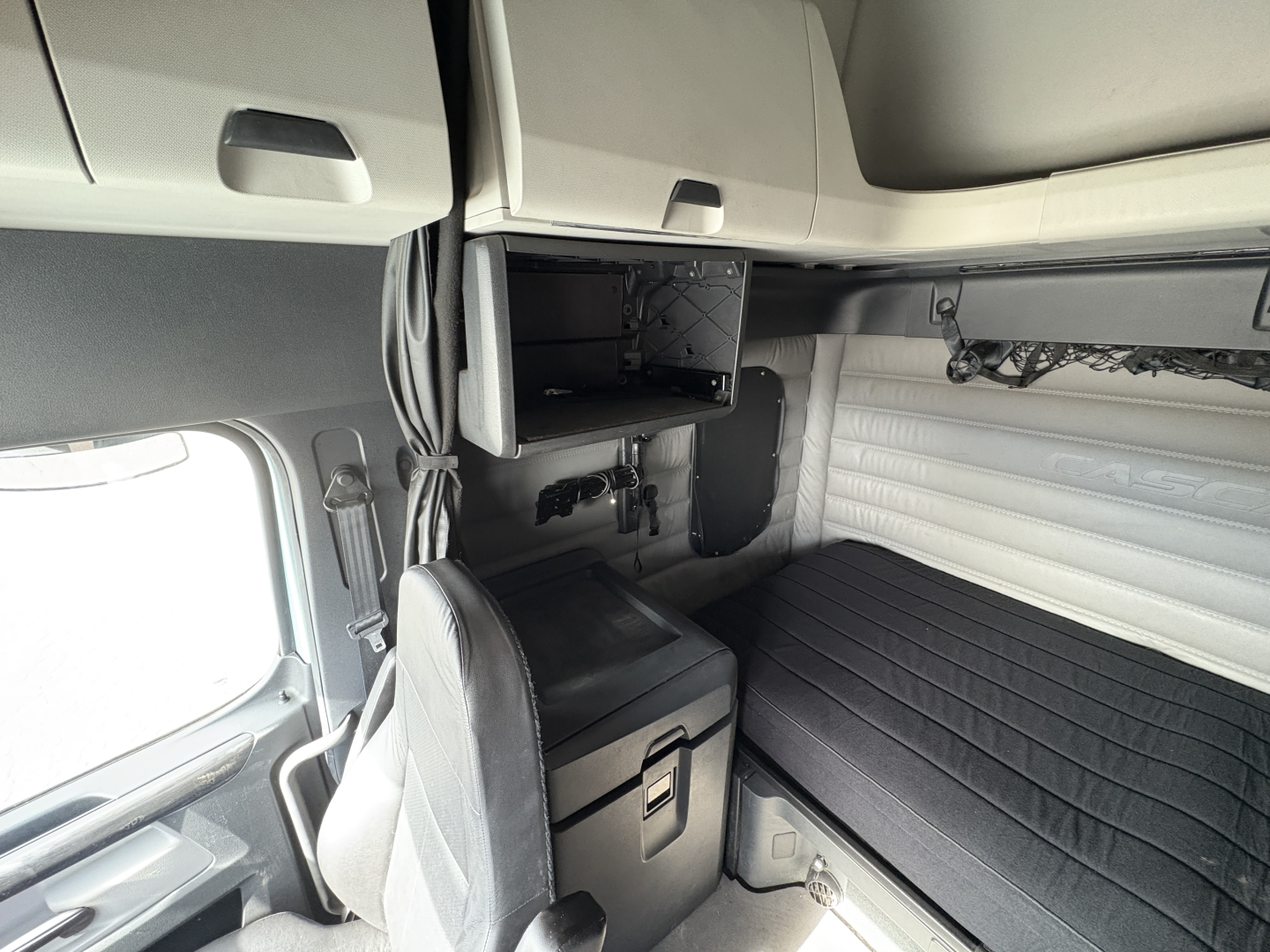 Freightliner Cascadia 126 sleeper cab interior showing overhead storage and bunk area with a chair and shelves.