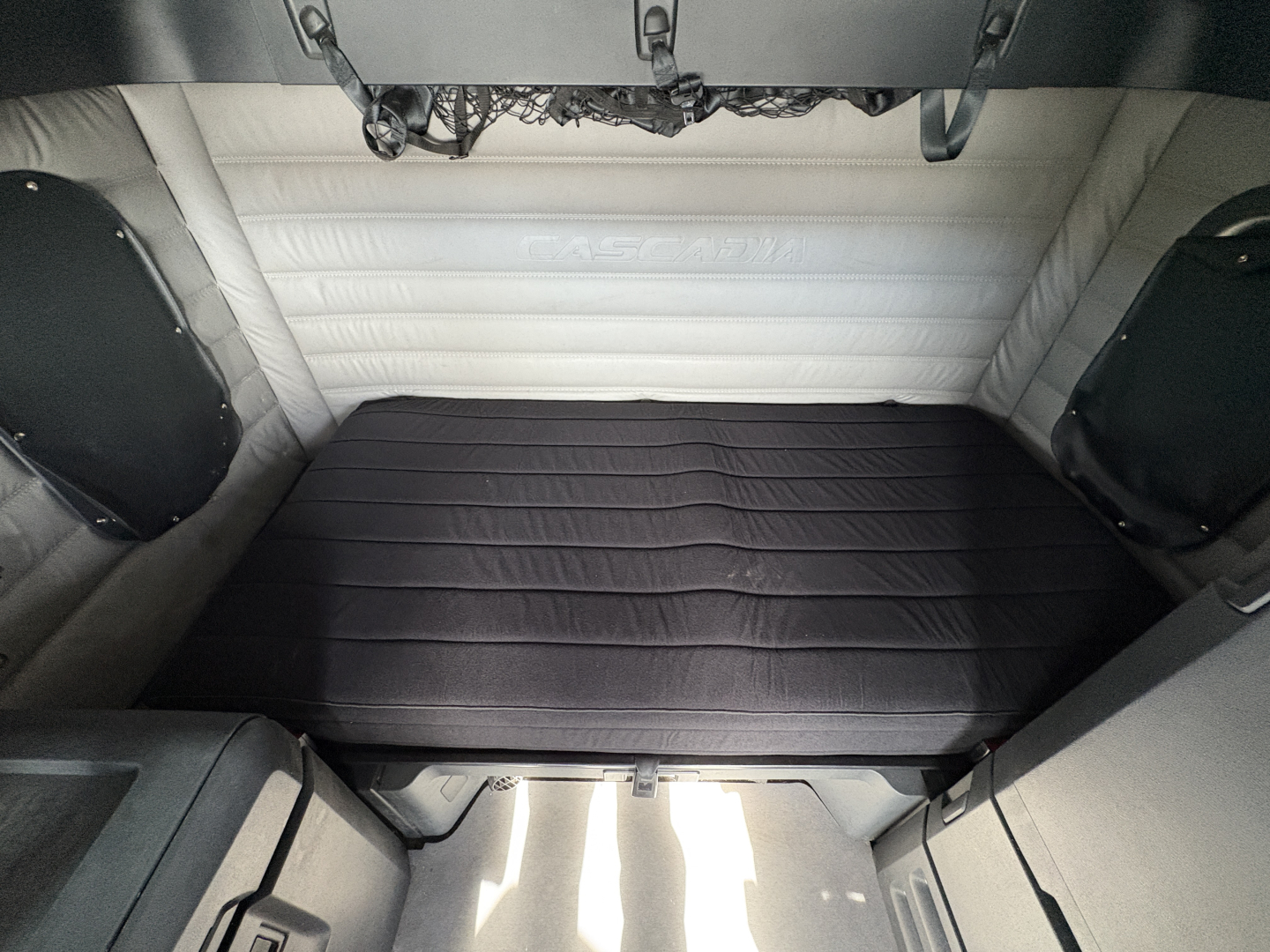 Freightliner Cascadia 126 sleeper cab interior with dark bed platform and light-gray padded walls.