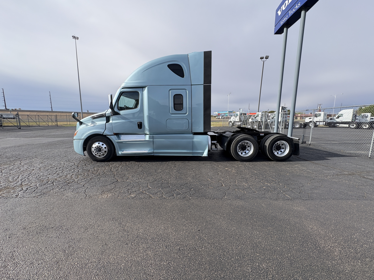Truck cab side view showing Freightliner Cascadia 126 sleeper with light blue paint and triple rear axles.