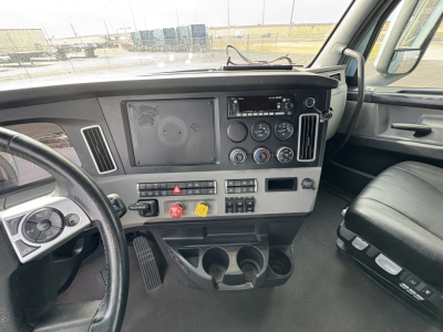 Cab interior of a Freightliner Cascadia 126 truck showing dashboard and steering wheel with gauges, controls, and cup holders.