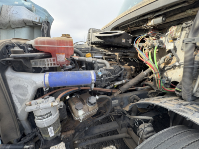 Freightliner Cascadia 126 engine bay showing coolant reservoir, blue silicone hose, air filter canister, and various wiring harnesses.