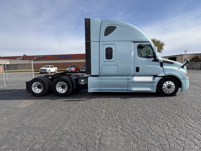 Semi tractor cab side view showing Freightliner Cascadia 126 with light blue paint, three rear axles, aerodynamic sleeper cab, side mirrors, and chrome steps.