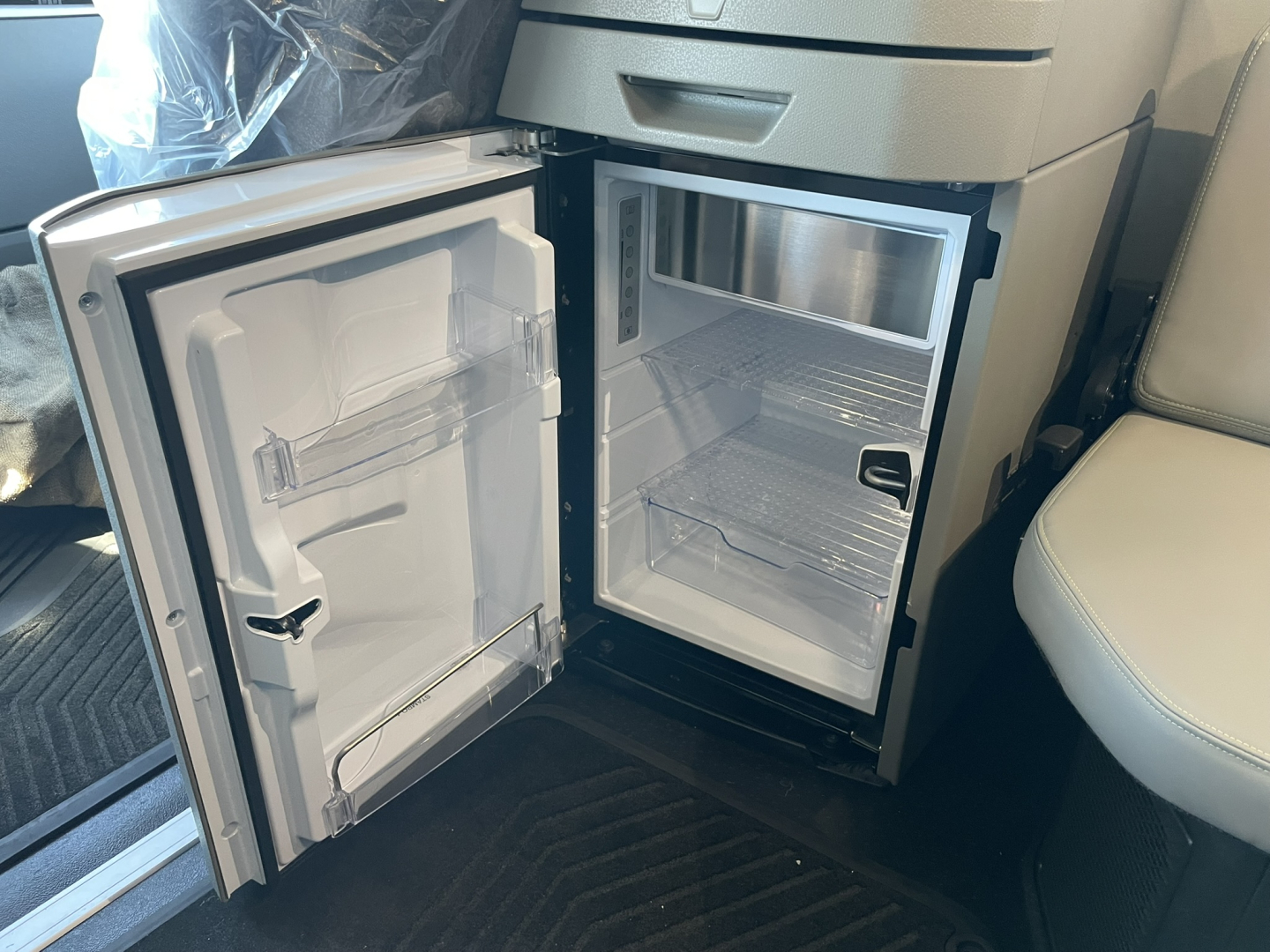 Volvo VNL64T860 truck interior showing open under-cab refrigerator and empty fridge shelves with door open.