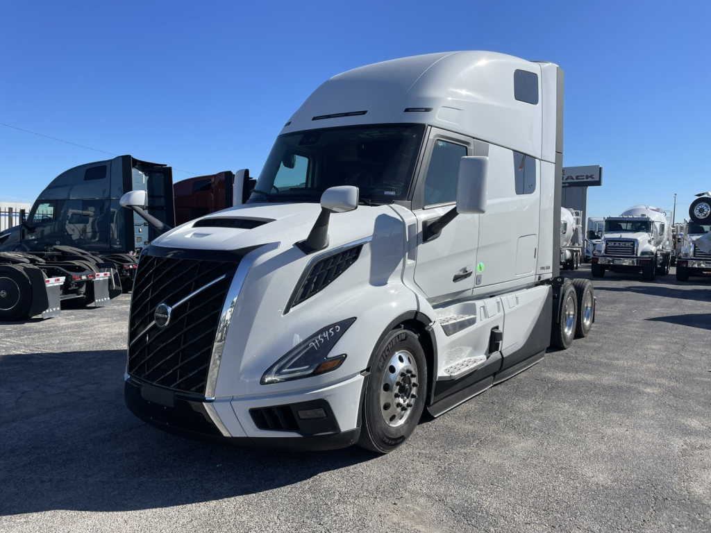 Volvo VNL64T860 sleeper cab in white showing front grille, headlights, side mirrors, and wheel with dual rear axles.