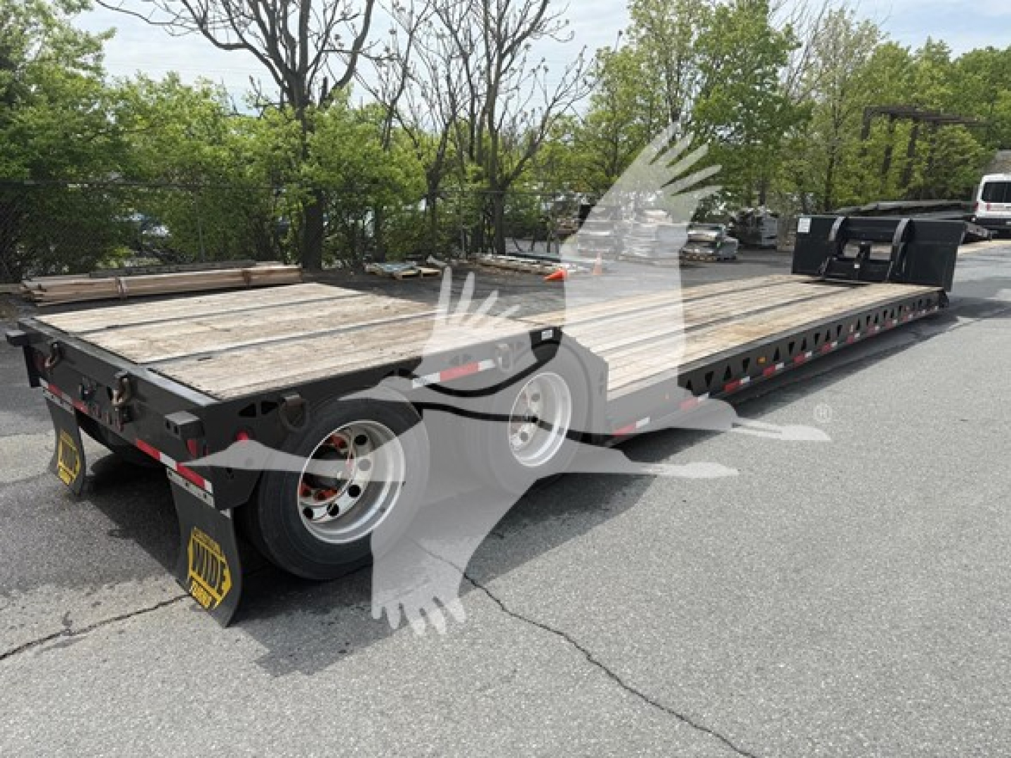 Talbert mechanical detach lowboy trailer showing wooden deck and dual rear axles with tires, I-beam frame, and worksite surroundings.
