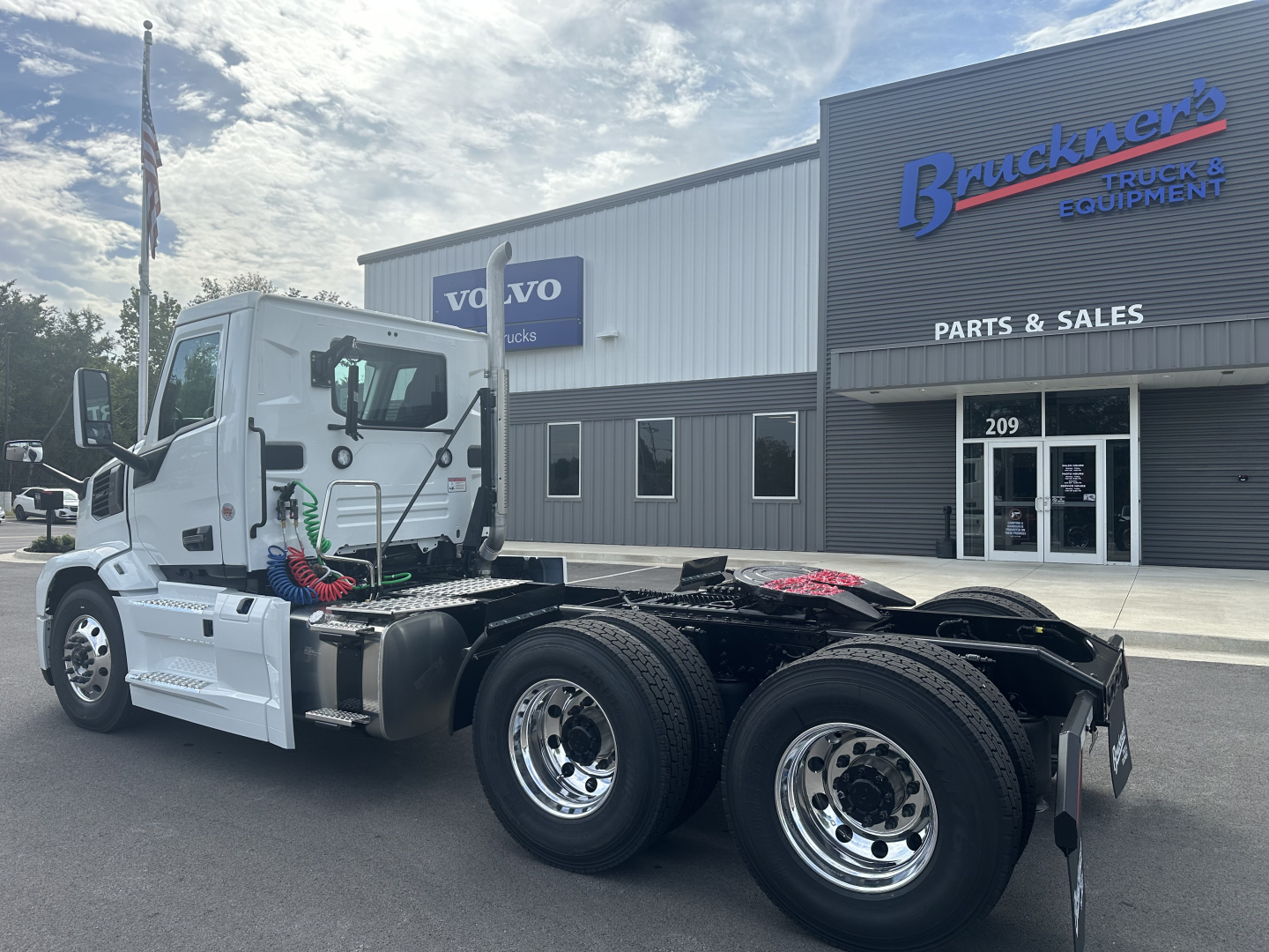 Mack PR64T truck cab and chassis in blue and white with Dakota wheels, viewed from left side with dealership building in background.