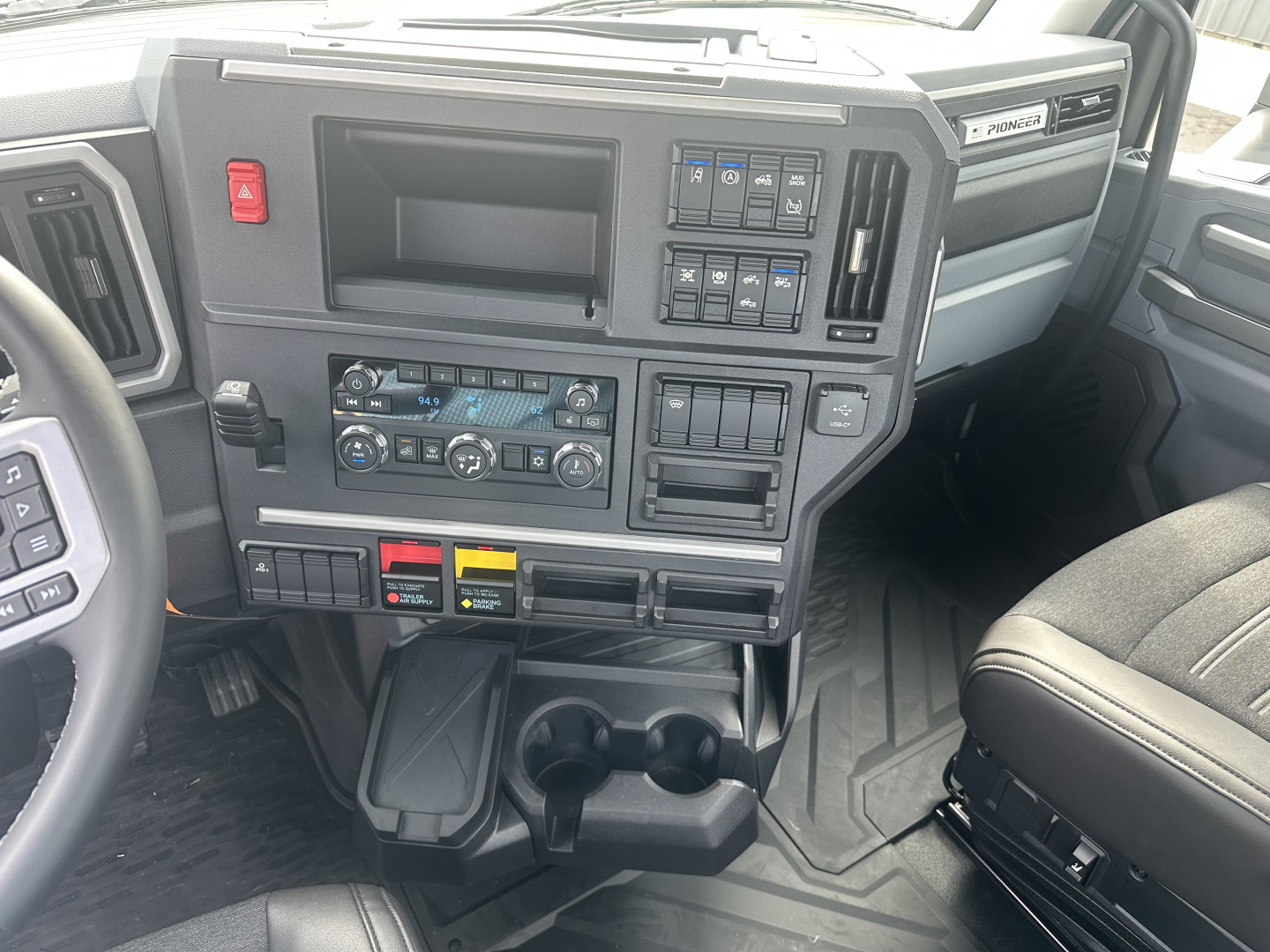Dashboard interior of a 2026 Mack PR64T showing center console with climate controls, switches, cup holders, and storage pockets.