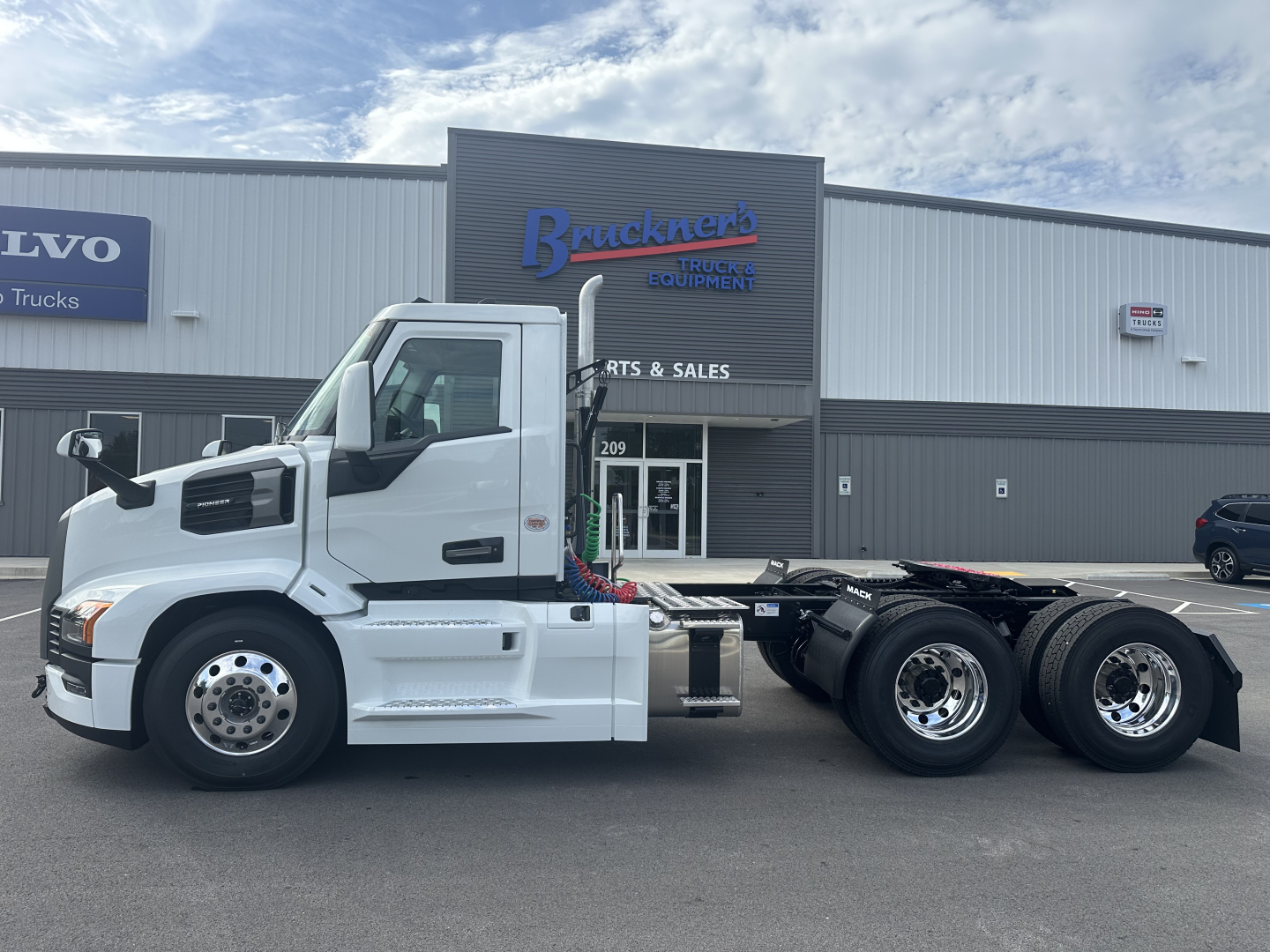Truck side view of a white Mack PR64T tractor in front of a dealership building with signage
