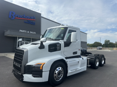 Mack PR64T tractor unit in white parked outside a truck dealership. Side view showing cab, mirrors, fuel tanks, steps, and dual rear axles with wheels.