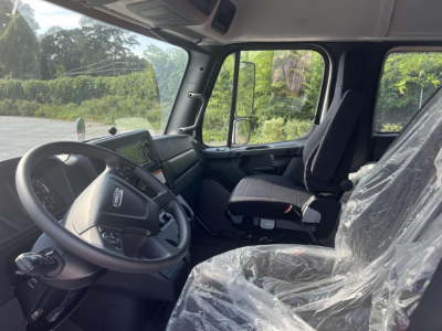 Cab interior of a 2027 Freightliner M2 106 Plus box truck showing steering wheel, dashboard, driver seat covered in plastic, and passenger seat with protective wrap.