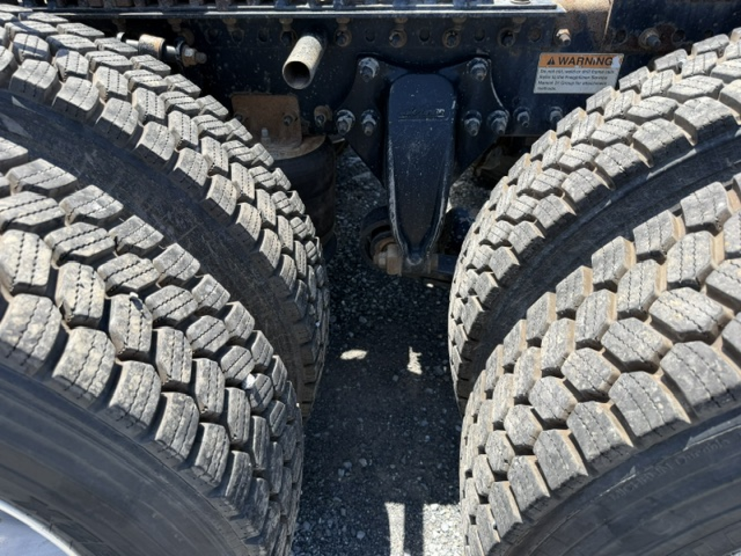 Freightliner Cascadia CA125DC drivetrain area showing twin rear duals and chassis components; close view of contact point between rear axles with suspension hangers and leaf spring mass; visible wheel tread blocks.