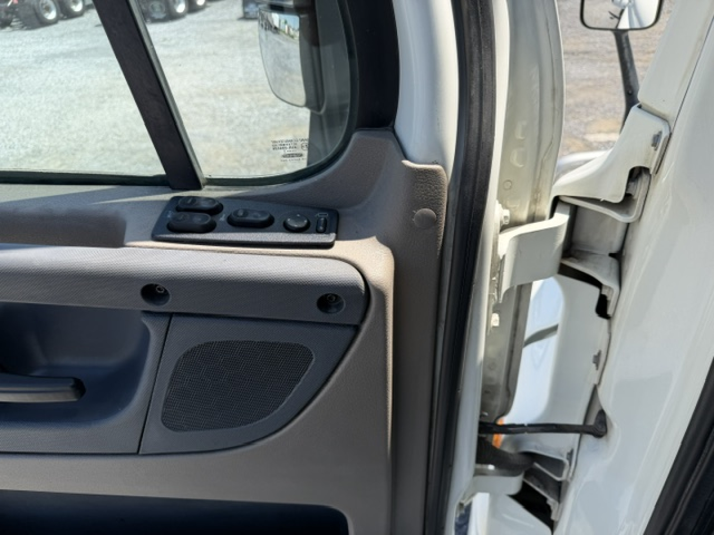 Freightliner Cascadia cab interior door panel and open driver door showing window controls and speaker grille.