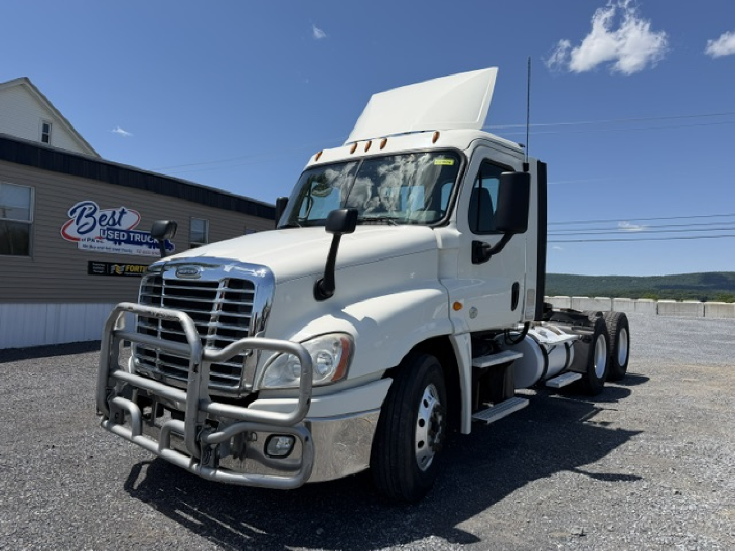 Front-left view of a white Freightliner Cascadia CA125DC tractor with a heavy-duty front bumper guard. Visible are the cab, hood, side mirror, and grille.