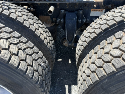 Freightliner Cascadia CA125DC drivetrain area showing twin rear duals and chassis components; close view of contact point between rear axles with suspension hangers and leaf spring mass; visible wheel tread blocks.
