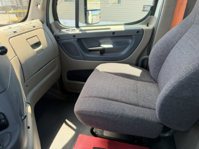Cab interior of a Freightliner Cascadia truck showing gray fabric seat, dashboard, and door panel in view.