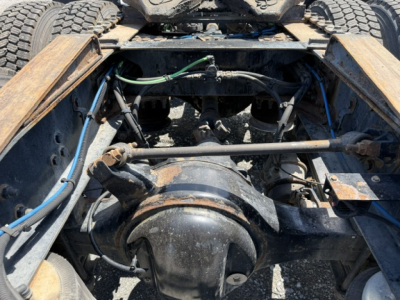 Rear-engine area showing drivetrain and axles of a Freightliner Cascadia truck frame with hoses and wiring visible.