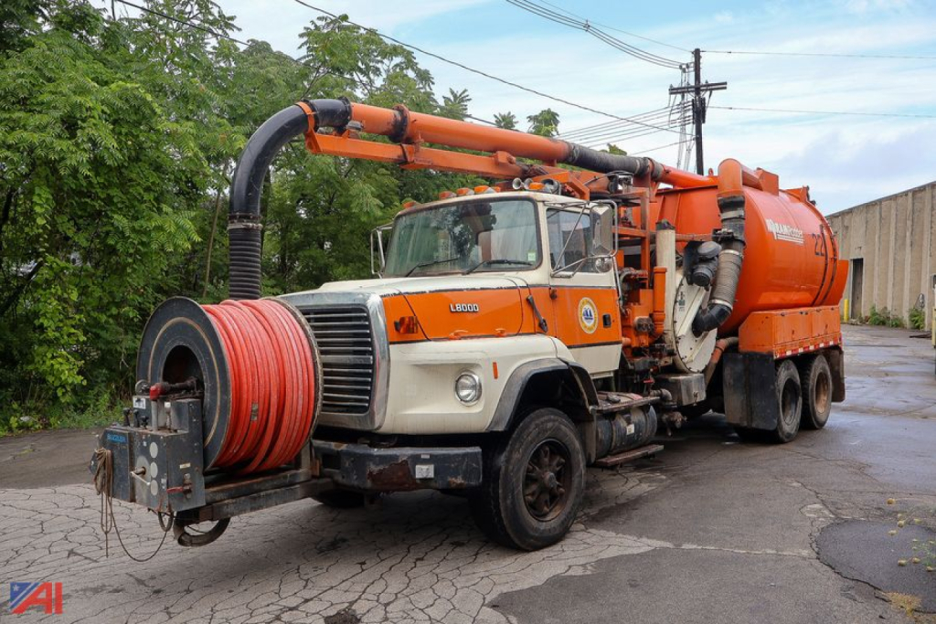 Ford LTS8000 sewer truck with large orange vacuum tank and hose reel in foreground.