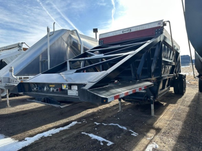 Bottom dump trailer in service showing air ride suspension and open-top discharge area with metal frame and rear loading chute.