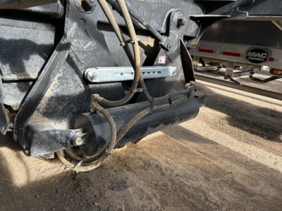 Bottom dump trailer frame with hydraulic lines and cylindrical actuator; visible metal brackets and hoses