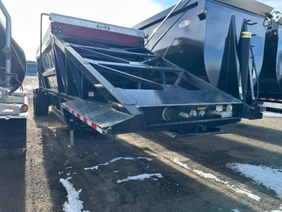 Bottom dump trailer with fold-down ramps and metal framework, viewed from rear-left showing loading bed and hitch area.