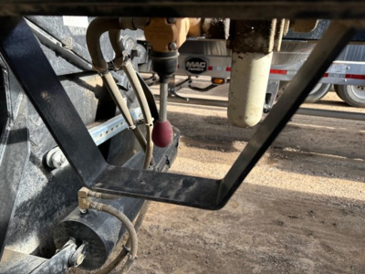 Bottom dump trailer undercarriage showing hydraulic cylinder, hoses, and frame with a MAC trailer brake actuator visible.