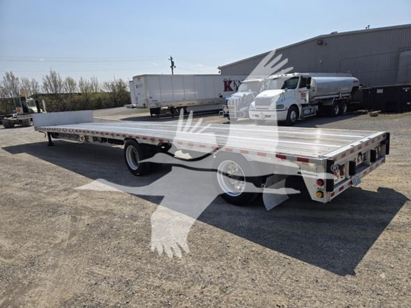 Flatbed trailer showing drop deck, dual rear axles, aluminum decking, and rear lighting; wheel fenders and gooseneck area visible.