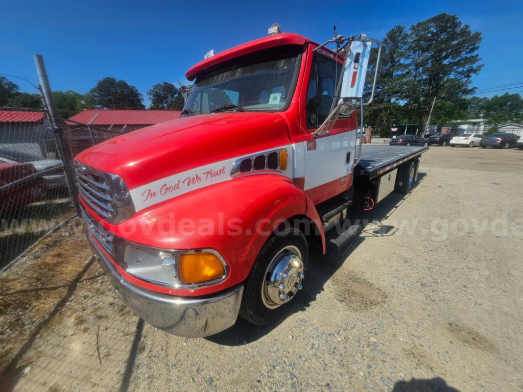 Tow truck front-left view showing red and white Sterling Acterra with flatbed, chrome bumper, and side text 'In God We Trust' visible.