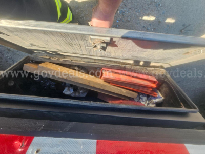 Truck bed storage showing toolbox with contents including manuals and a red item, open lid with reflective stripe visible.