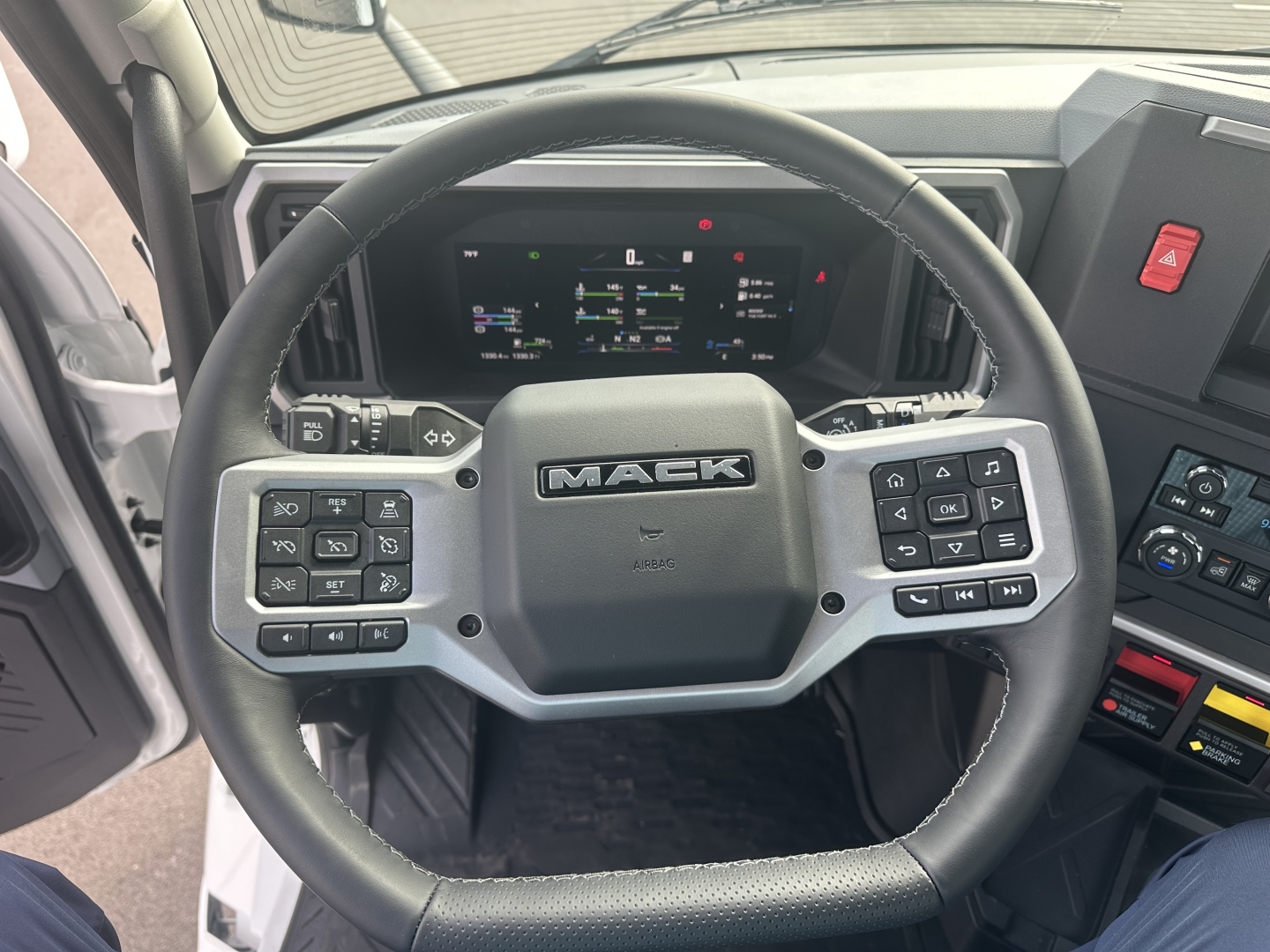 Mack PR64T truck interior showing steering wheel with Mack logo and digital instrument cluster.