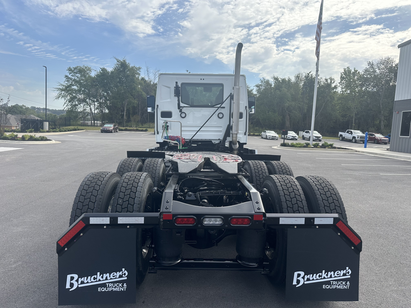 Truck chassis and cab of a 2026 Mack PR64T in a dealership lot. Dual rear axles, fifth wheel area, exhaust stack visible, rear view showing mud flaps with Bruckner's branding.