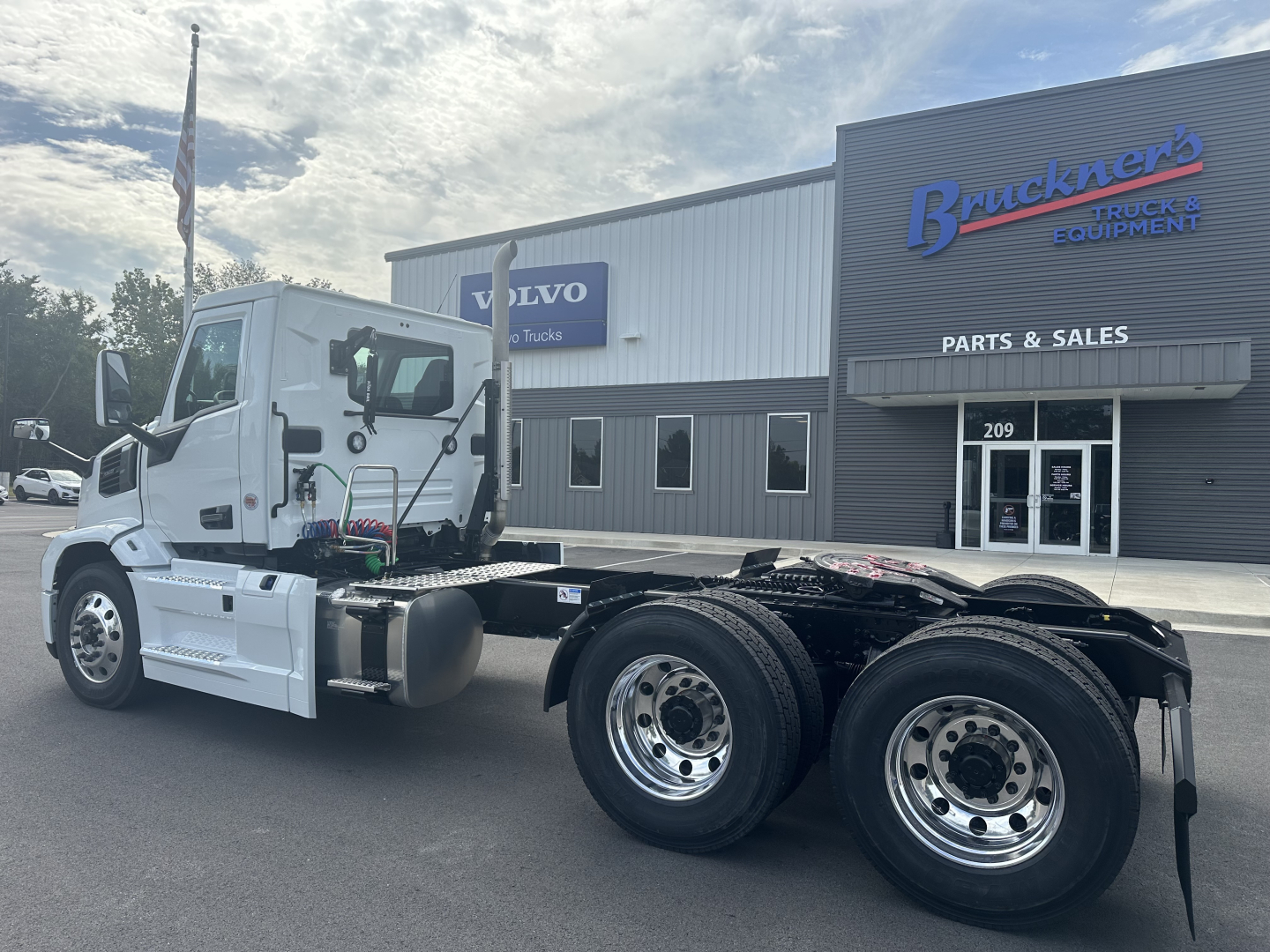 Truck chassis with cab and dual rear axles in front of a dealership building.