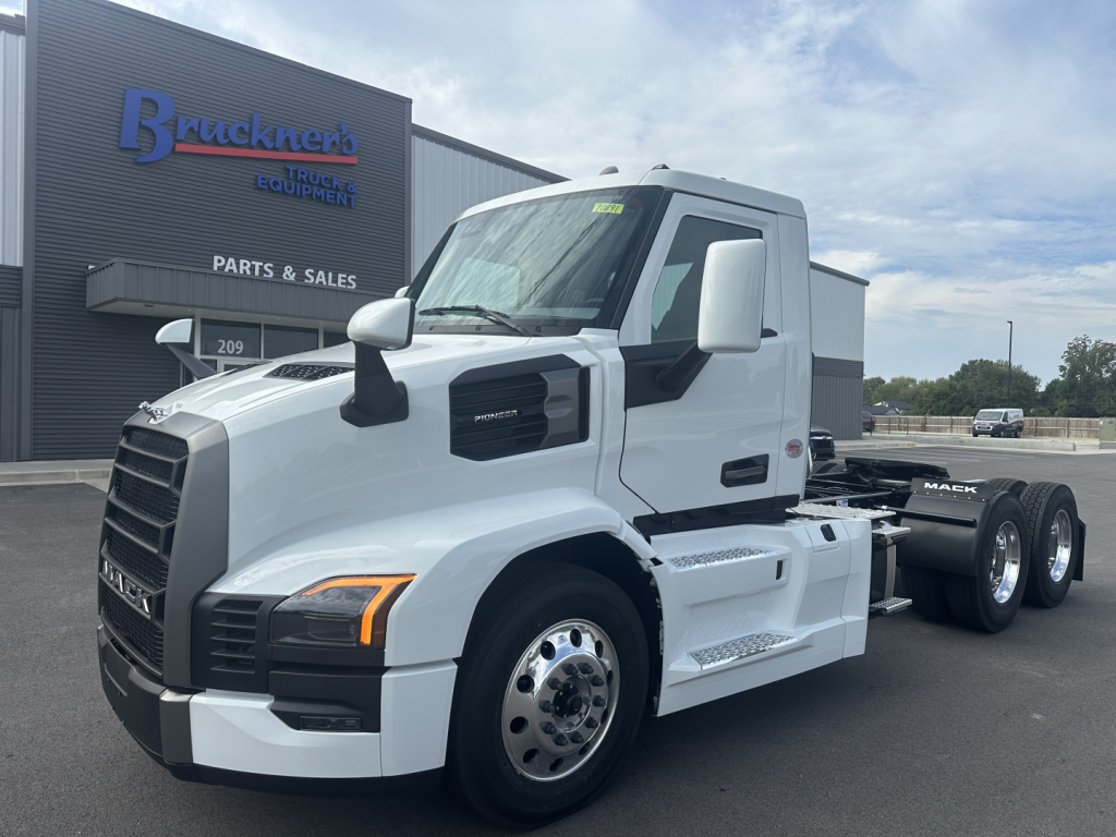 Mack PR64T truck front/side view in a dealership lot with white cab and black grille Fitted with dual rear axles and front fender mirrors.