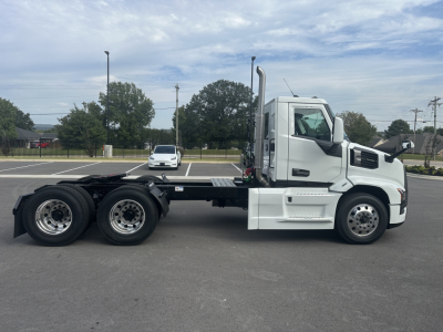 Truck side view showing a white 2026 Mack PR64T conventional daycab chassis with dual rear axles and mounted fuel/cargo area; VIN tag visible in listing.