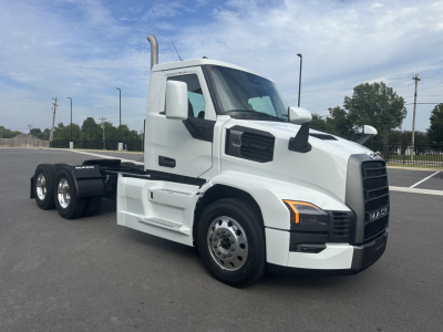 Conventional daycab truck in white showcasing Mack PR64T cab with extended hood and dual rear axles, side steps, and chrome wheels.
